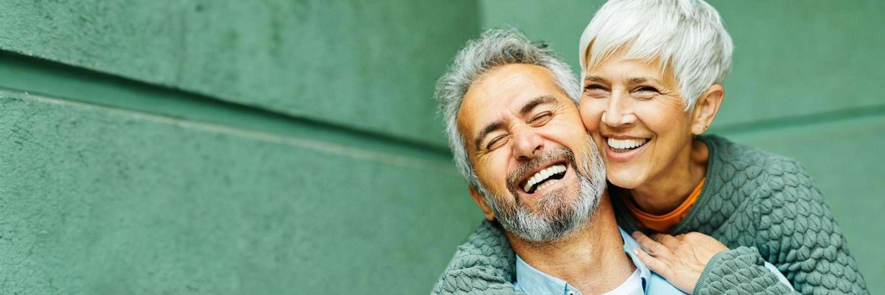 Happy older couple laughs, their smiles showcasing beautiful teeth, perfect for veneers.