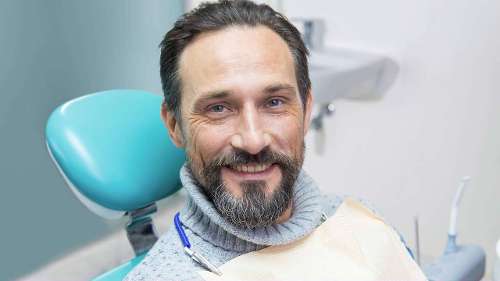 A man smiling while sitting on a dental chair, showing healthy teeth after receiving dental fillings